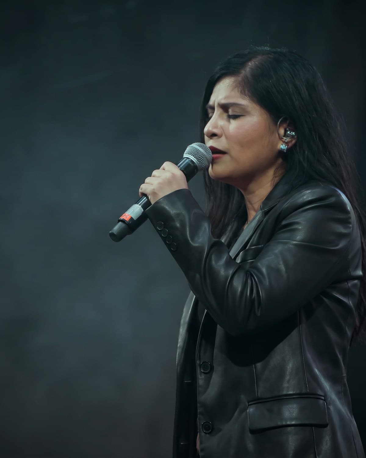 Genesis Campos singing into a handheld microphone on a darkened stage
